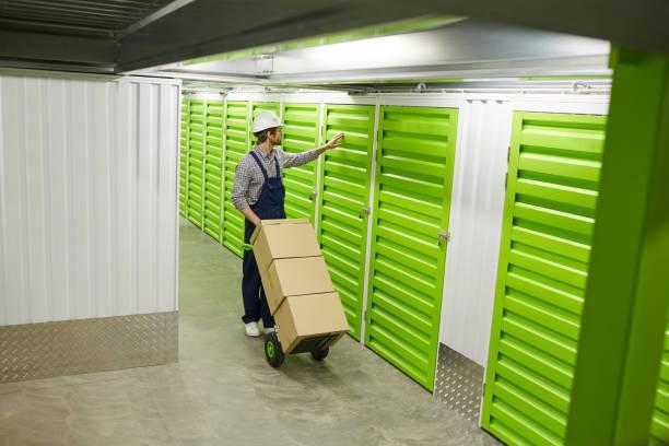 Worker with load in storage room Worker in working clothing standing with cart full of boxes and opening door of storage room Optimizing Supply Chains: The Role Of Cold Storage Services stock pictures, royalty-free photos & images