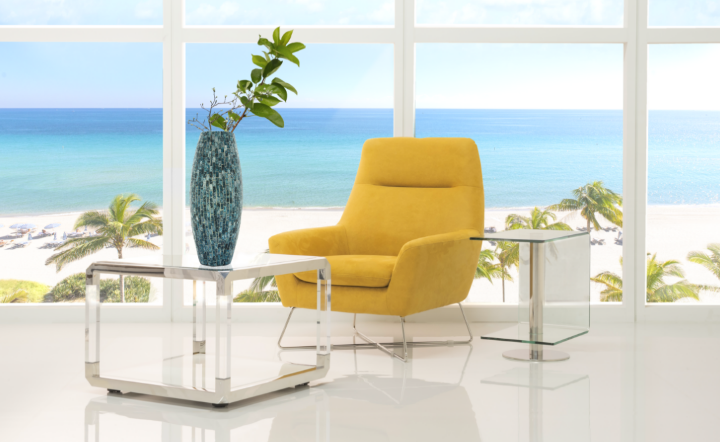Yellow accent chair in a room with a large coffee table and a small side table and beach views.