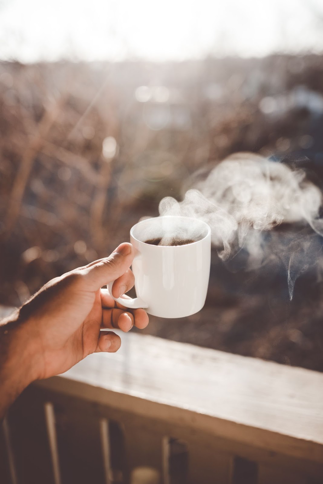 Picture of a someone holding a cup of coffee on a deck, with steam pouring off the cup of coffee