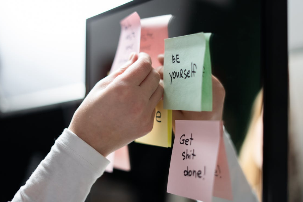 Hand reaching to place sticky note on refrigerator with the words Be Yourself and Get Shit Done!