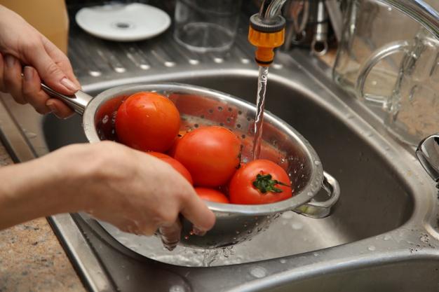 A women using a colander and a kitchen sink to wash tomatoes. Free Photo