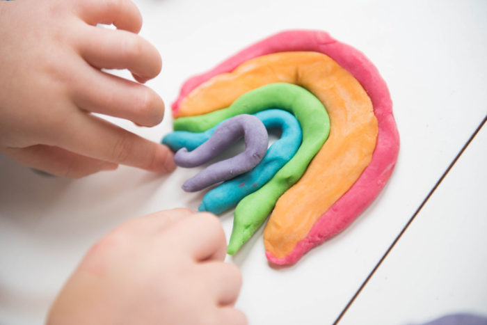 A child making a rainbow with multiple colors of playdough.