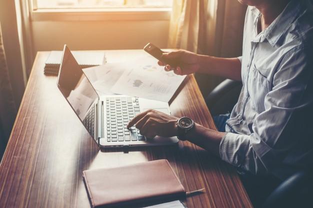 Businessman hands using cell phone with laptop at office desk. Free Photo