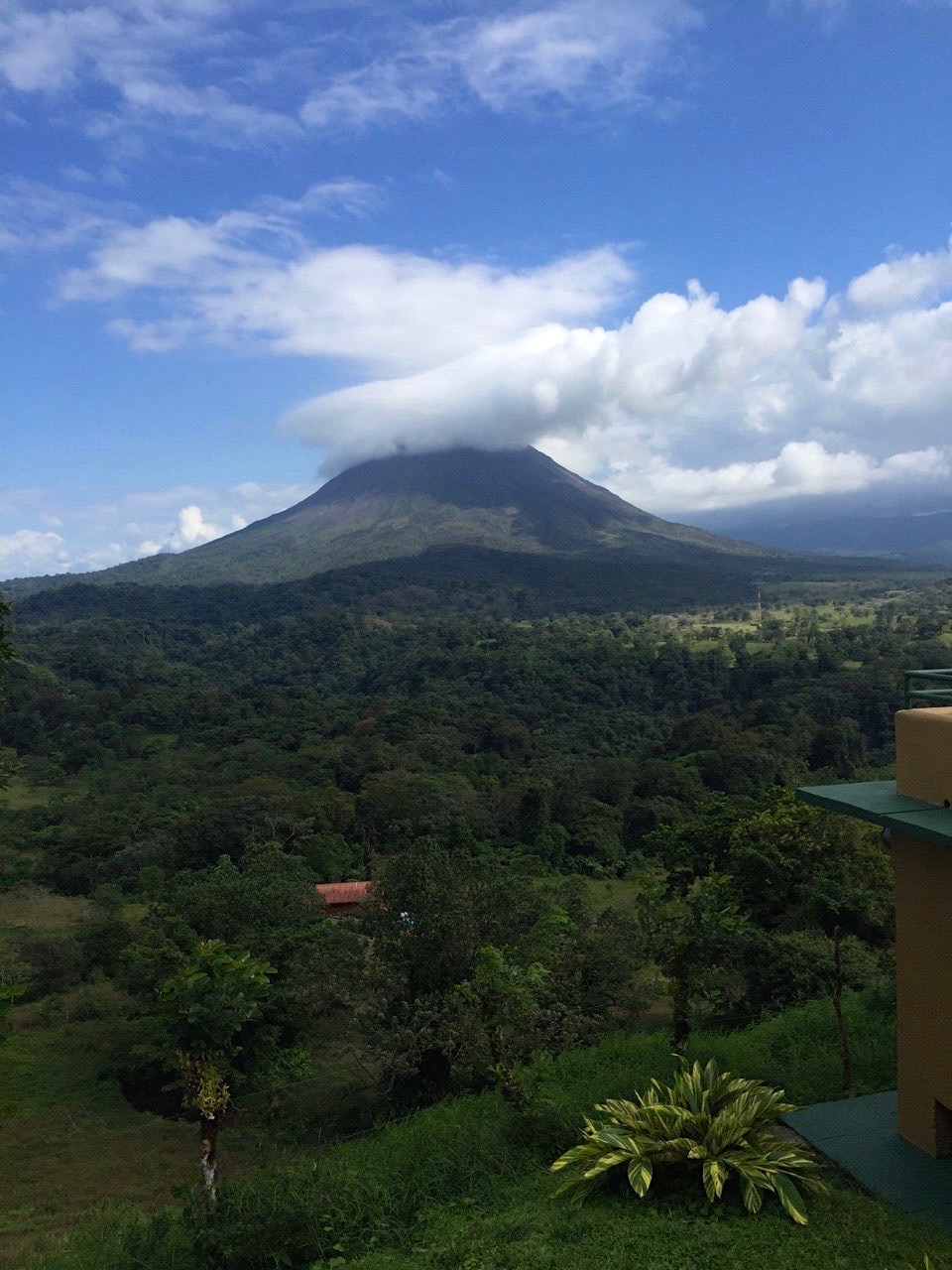 Large arenal volcano mountain seen from a nearby rain forest. The tip of the volcano is covered by large white clouds, seen on a sunny day in costa rica.
