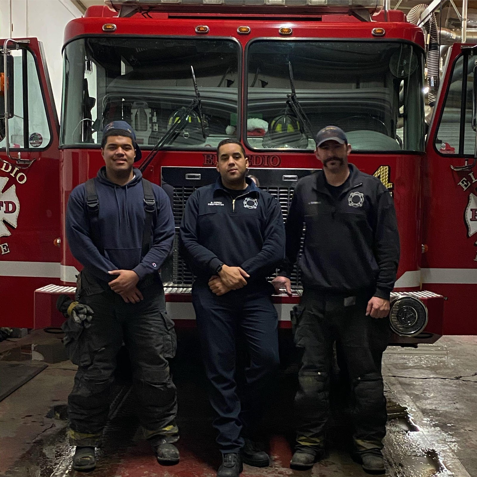 Three firefighters standing in front of a fire truck. 