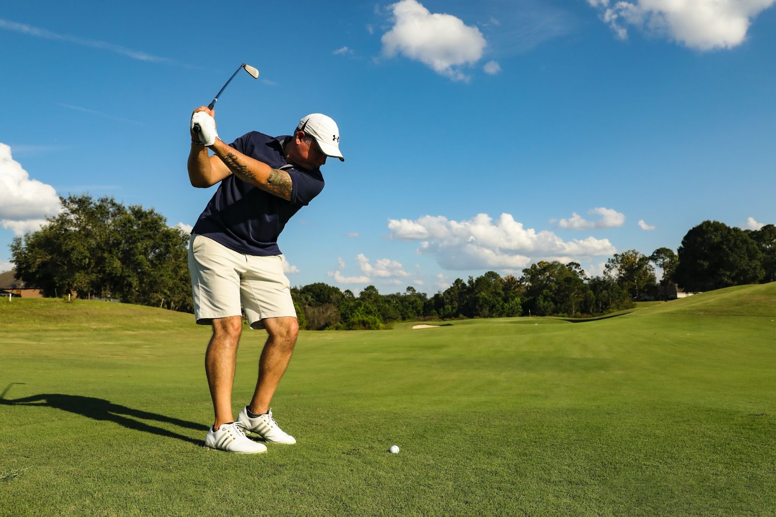 Man at a golf course swinging his club on a sunny day.