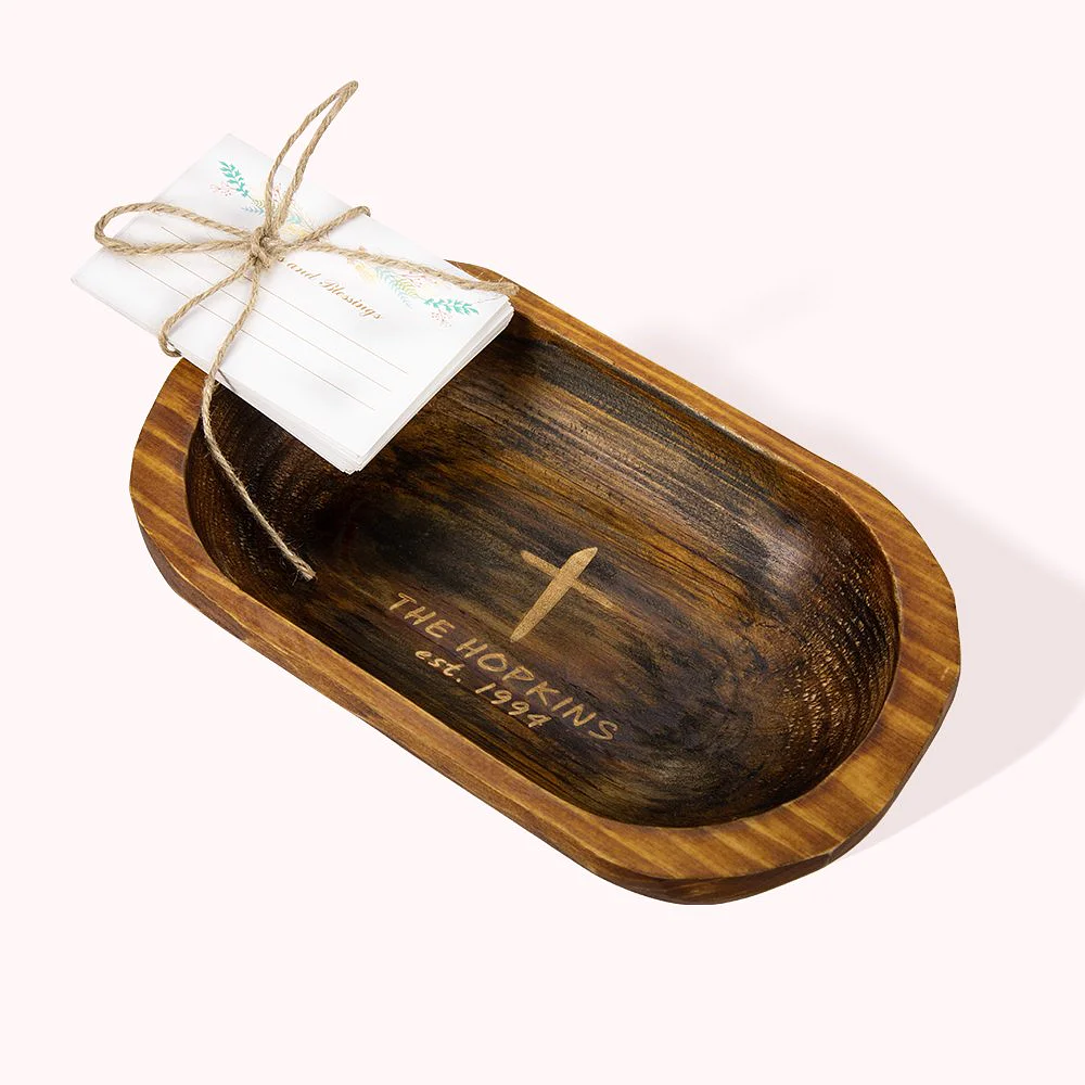 Bol à prière en bois de pin gravé d’une croix sous laquelle se trouve un nom et une date. Le tout est surmonté d’une feuille de papier placée sur le bord du bol, pliée et fermée par une cordelette.
