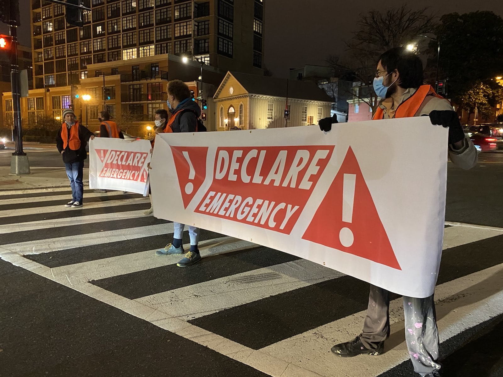 Five young protestors hold declare emergency banners across a road on what looks like a cold Washington DC night