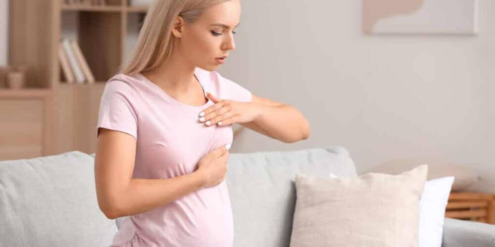 Une femme en train de récupérer après une chirurgie d'augmentation mammaire, assise sur un canapé avec des coussins de soutien autour d'elle.
