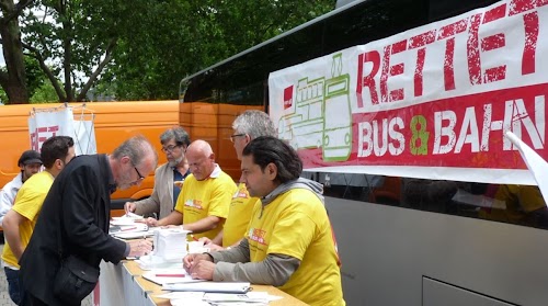 Kolegen an Tisch mit Unterschriftslisten, dahinter Transparent: »Rettet Bus & Bahn«.