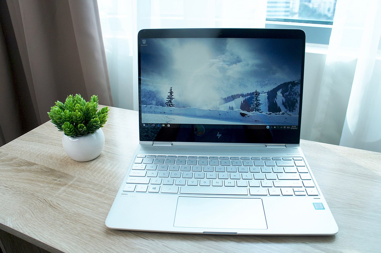 HP Envy x360 laptop is in the table with a artificial plant tree in white color.