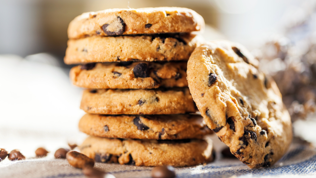 six stacked chocolate chip cookies with one leaning on the right side of the stack.