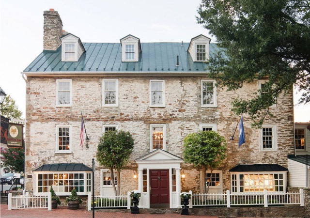 The historic Red Fox Inn & Tavern in Middleburg, Virginia. The three-story colonial-style building is made of stone with a metal roof, over a dozen front-facing windows, and a large red door.
