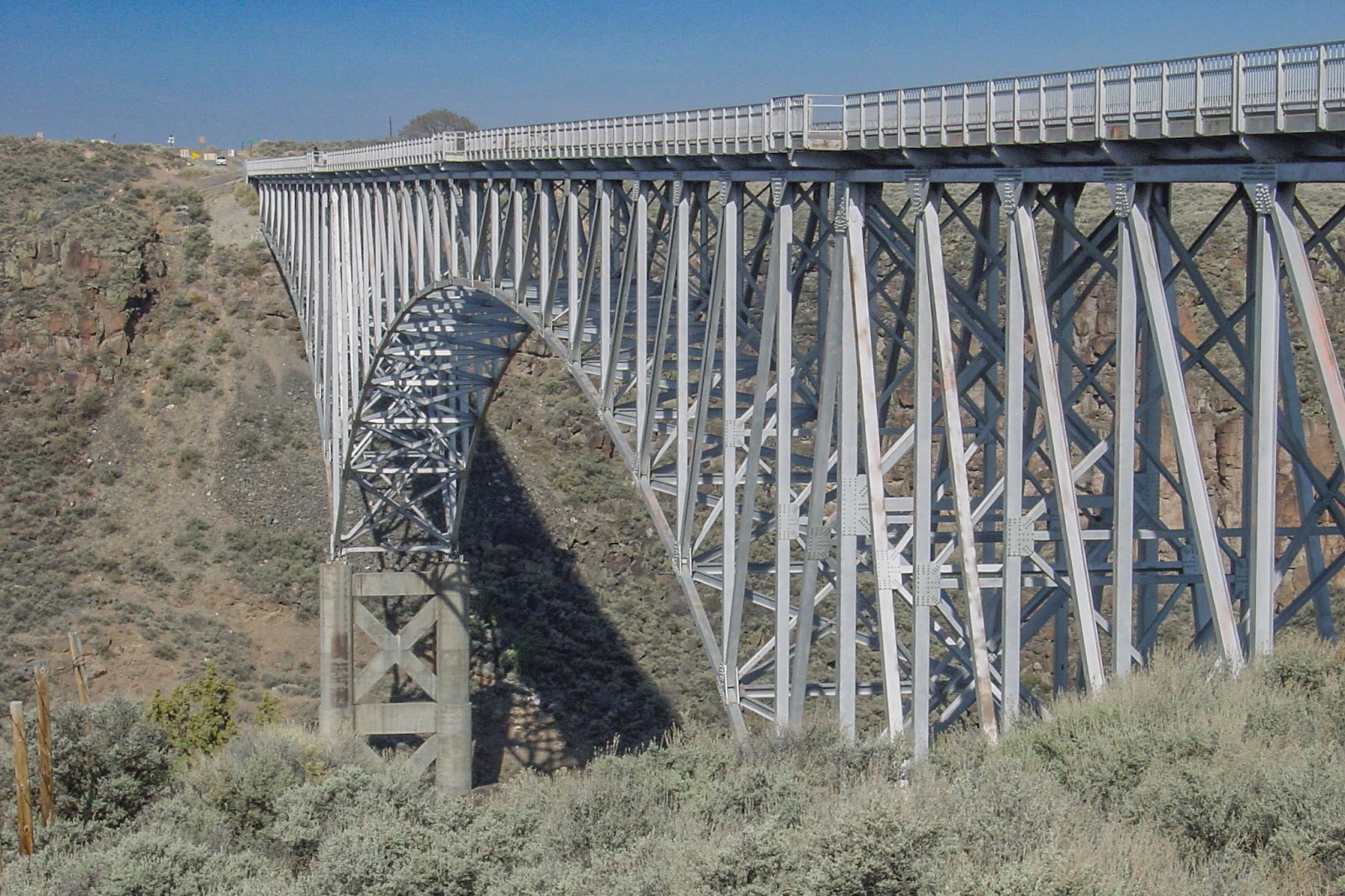 A bridge of steel and concrete arc over a canyon. 