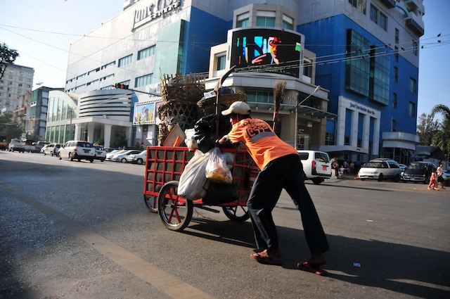 A man pushes a cartful of garbage near a busy intersection in Yangon. The 56-billion-dollar economy is growing at a steady clip of 8.5 percent per annum, but the riches are obviously not being shared equally. Credit: Amantha Perera/IPS