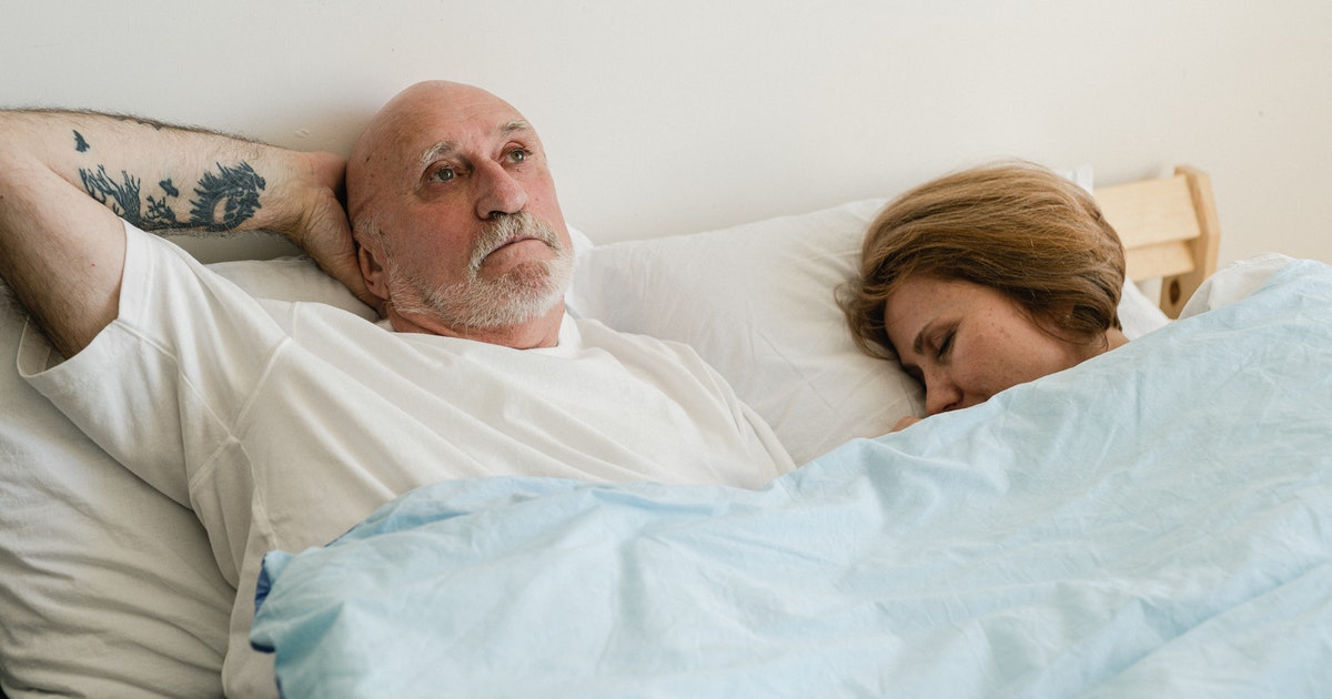 Elderly man awake under blanket unable to sleep