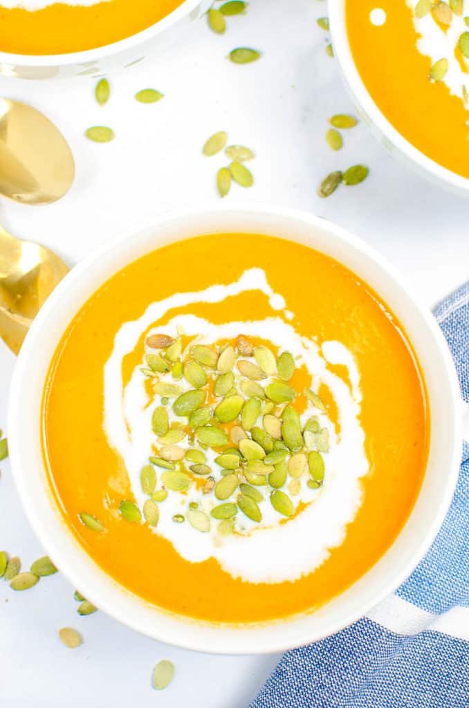 Carrot ginger soup in a white bowl topped with pumpkin seeds and coconut cream.