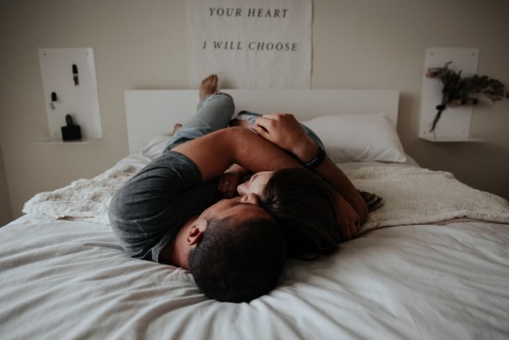 Hombre y mujer acostados y abrazados en cama con sábanas blancas