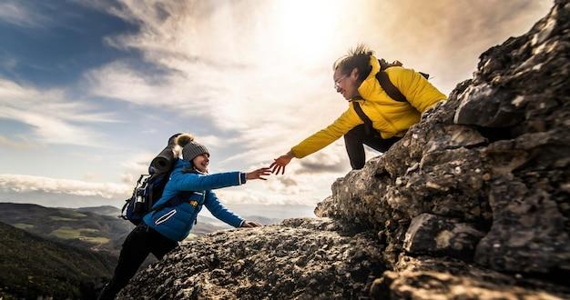 People helping each other hike up a mountain at sunrise giving helping hand and teamwork concept