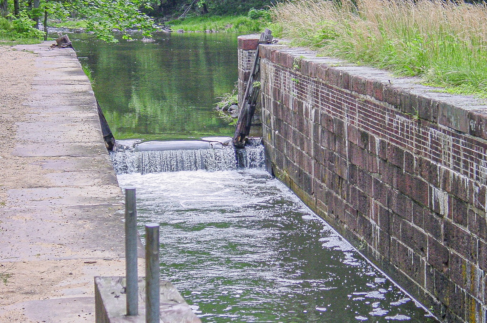 Water trickles over one end of a narrow channel with thick bricks on either side. 