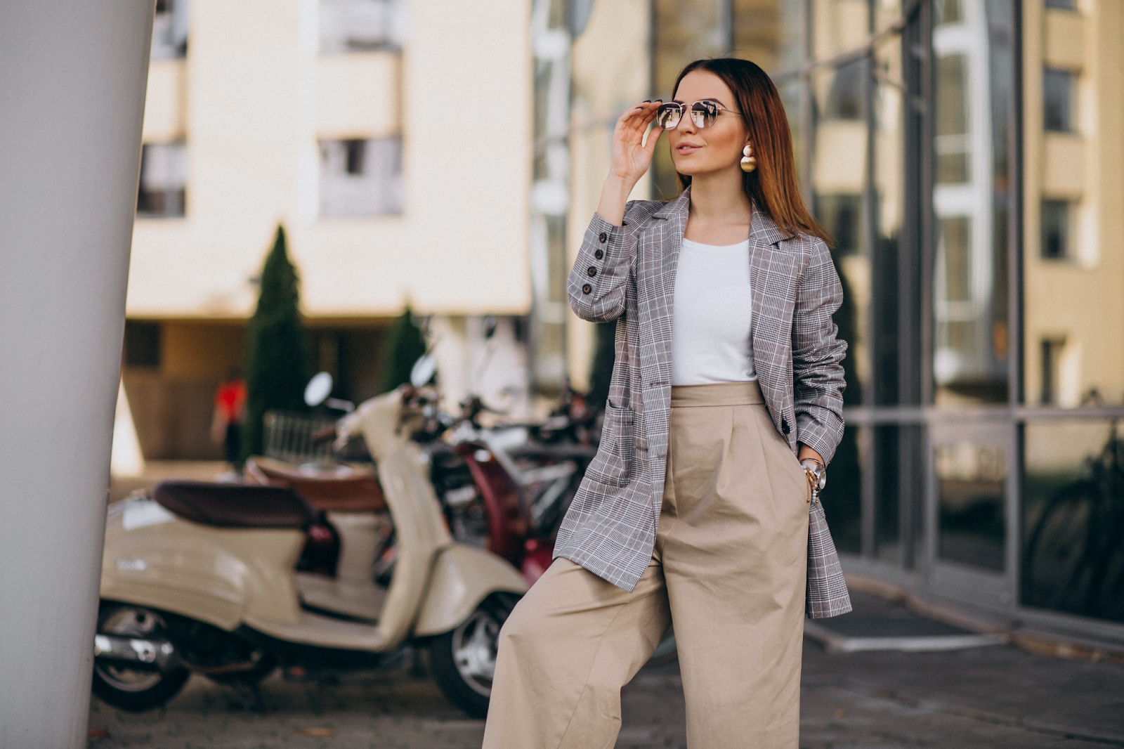 mulher de pé na rua na rua usando calça de alfaiataria e um blazer cinza por cima de uma blusa básica branca