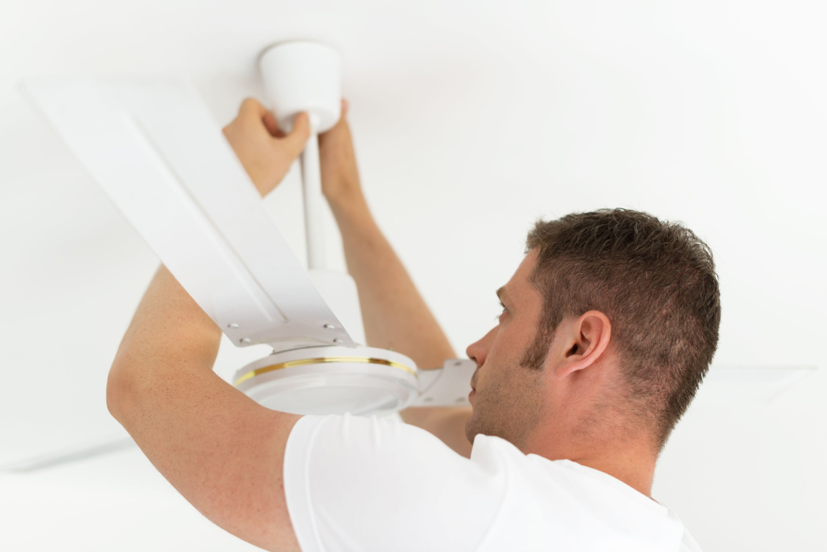 A man adjusting a ceiling fan.
