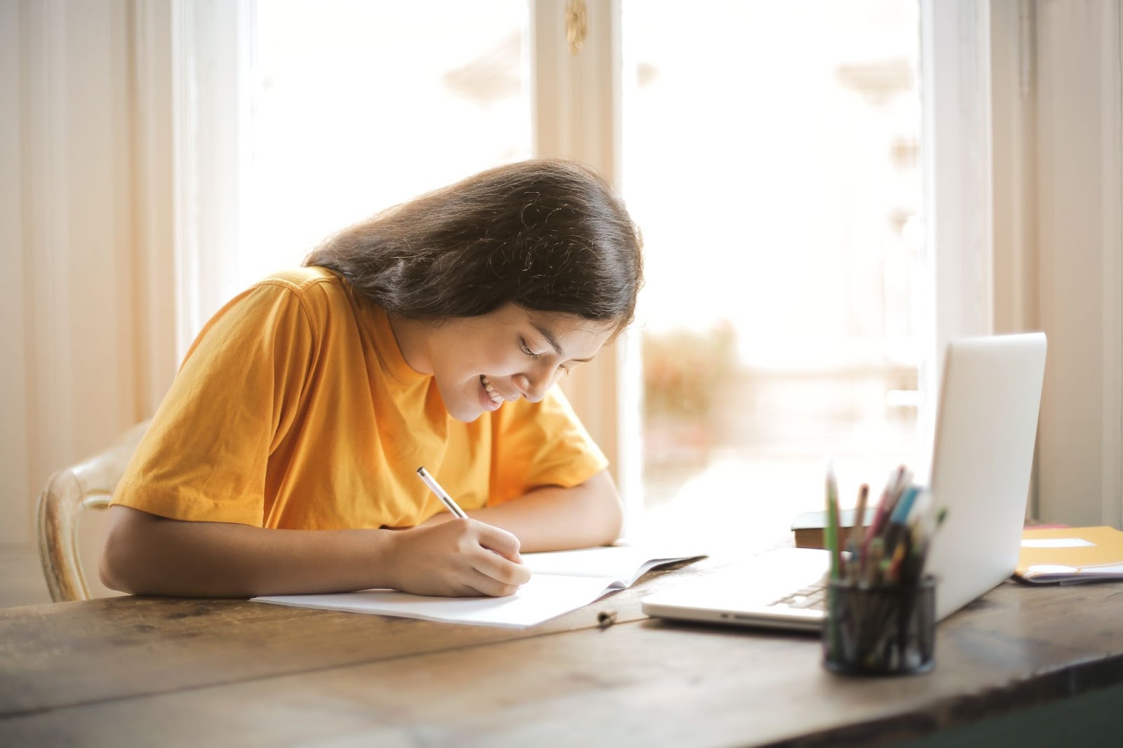 A girl in a yellow shirt writing on a book: What are MBA qualifications you should know? 