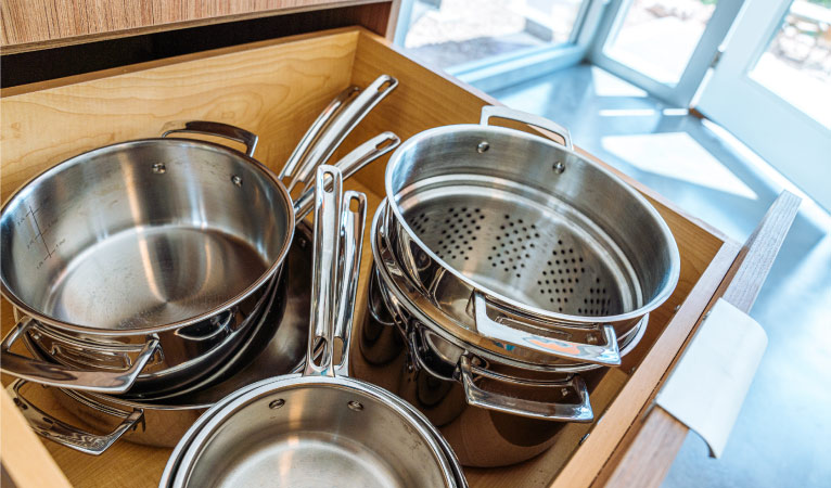 Pots, pans, and a colander in an open kitchen drawer.