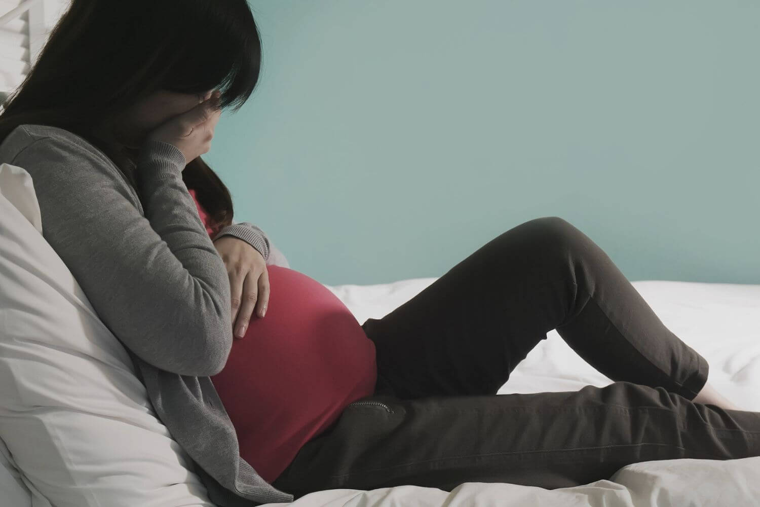 Pregnant woman sitting on a bed crying