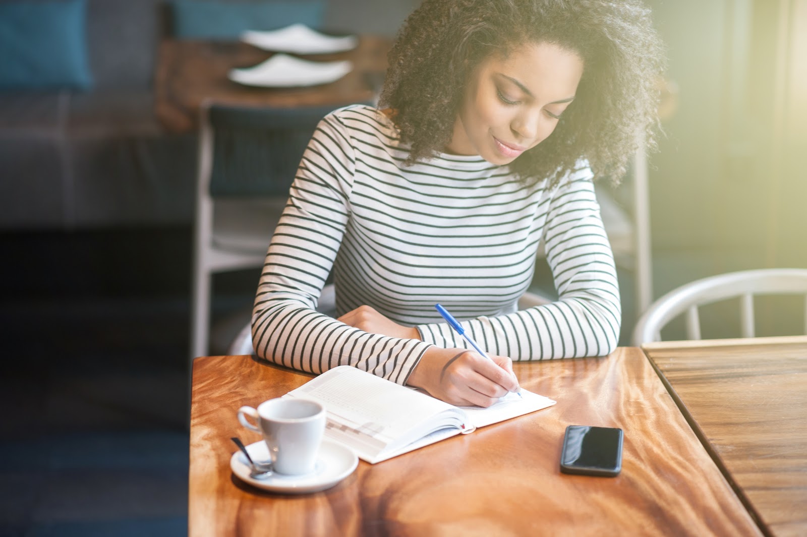 A woman writes in a notebook while at a coffee shop.