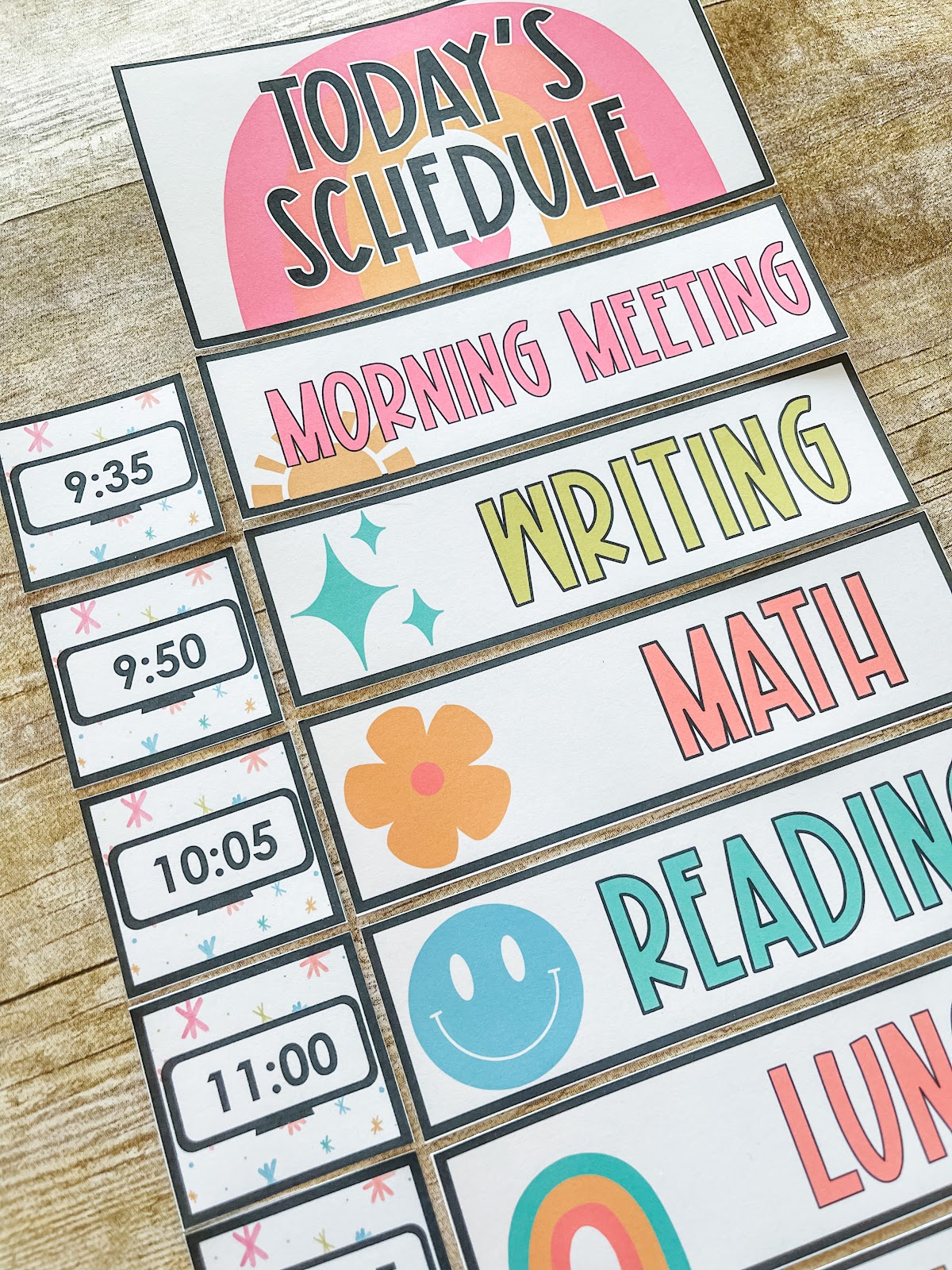 This image shows a close-up of a classroom schedule. There are small cards to the left-hand side with times displayed on a digital clock. The other cards have subjects like "Morning Meeting" or "Math" written on them. All of these cards have icons and bright colors. 