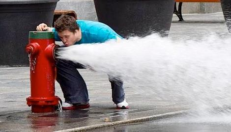 A guy trying to drink out of a blasting fire hydrant