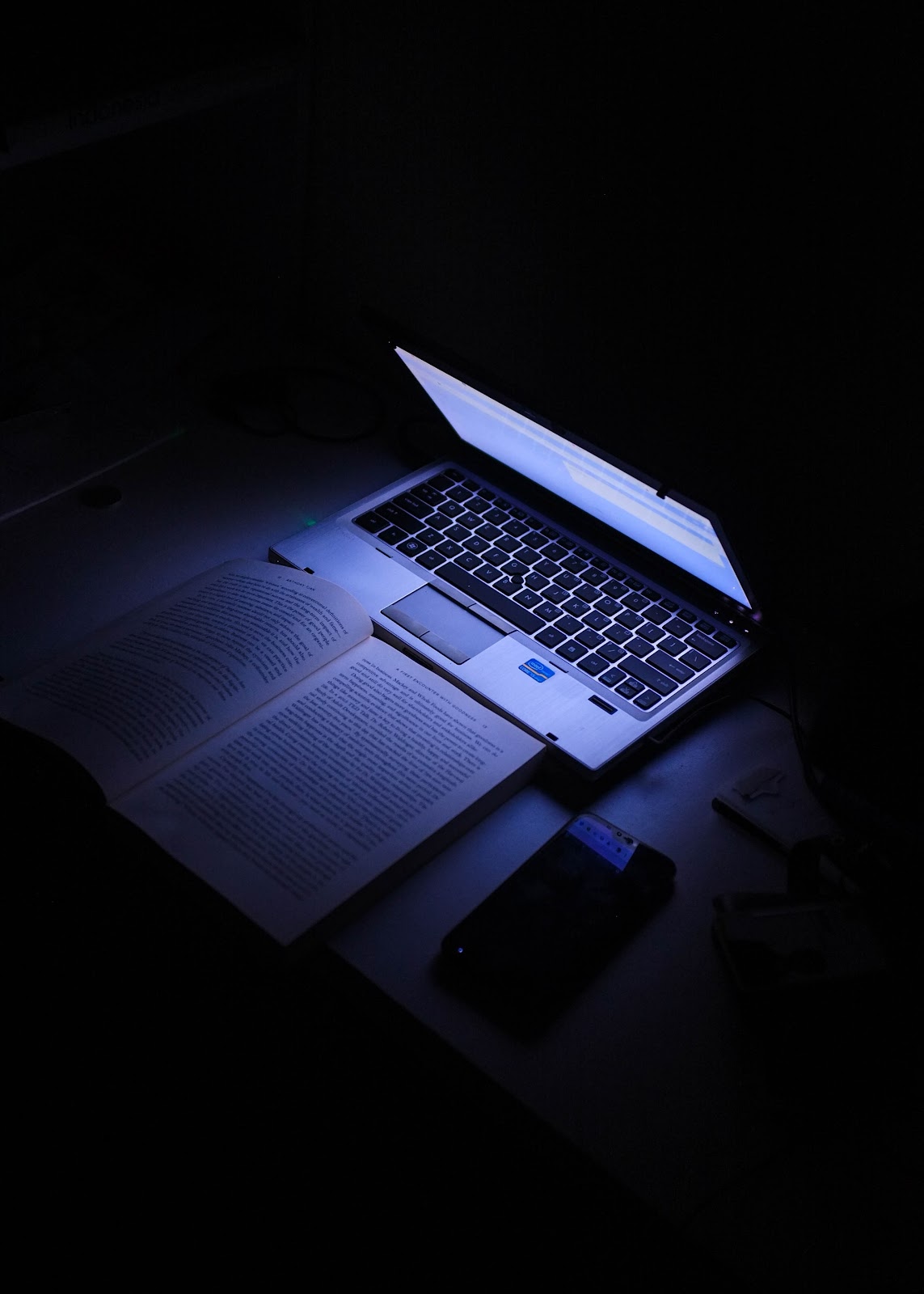 a laptop screen lights up the darkroom and pages of a book