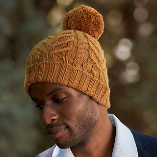 man wearing a dark yellow cable knit hat with a matching yarn pom pom