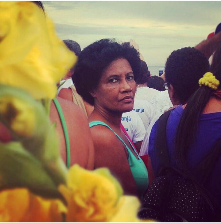 Mulher negra, olhando para fotografia, com feições serias. Ela está em um culto a Iemanjá em Copacabana, Rio de Janeiro.