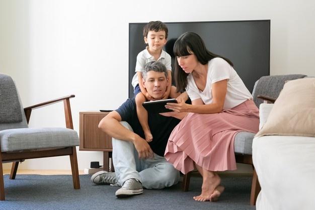 Casal família e filho usando tablet digital, olhando para a tela, sentado na sala de estar.