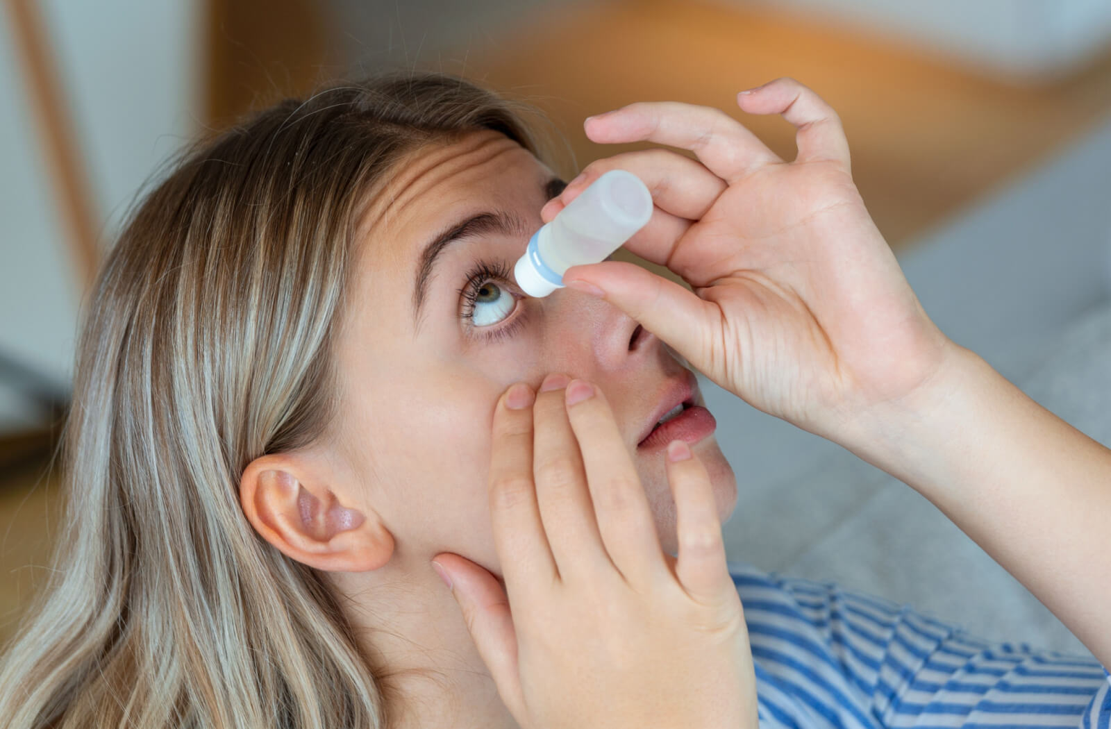 A young woman pulling down her right eyelid to apply artificial tears to her eye