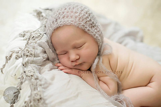 newborn wearing a tan bonnet and lying on a pillow