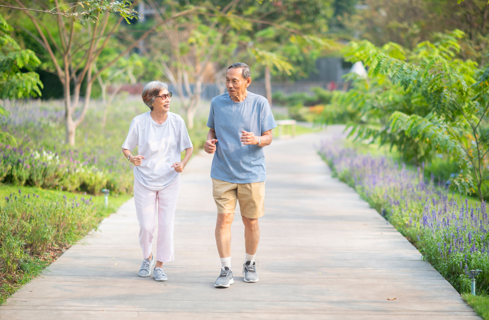 A senior woman and a senior man smiling while walking outdoors.