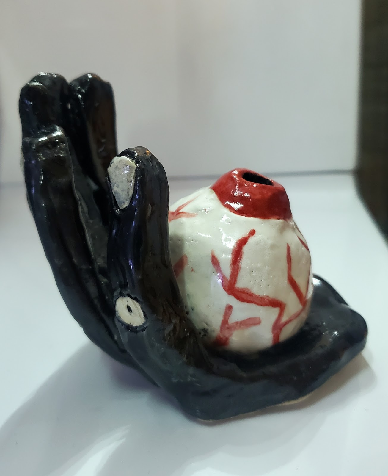 A ceramic of a black hand holding an eyeball that is red with lots of veins.