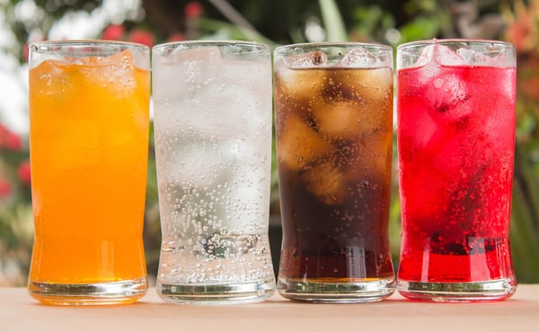 Four glasses full of ice filled with four different flavors of soda