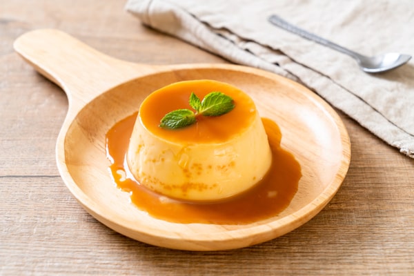 Caramel pudding with mint leaf on top, served on a wooden plate
