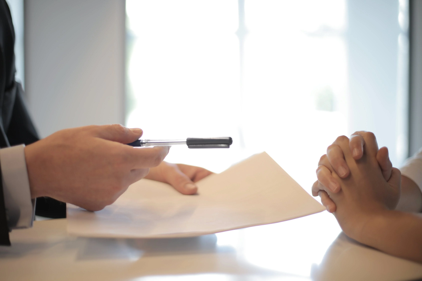 Hands of mortgage lender conversing with an applicant over a table in an office.