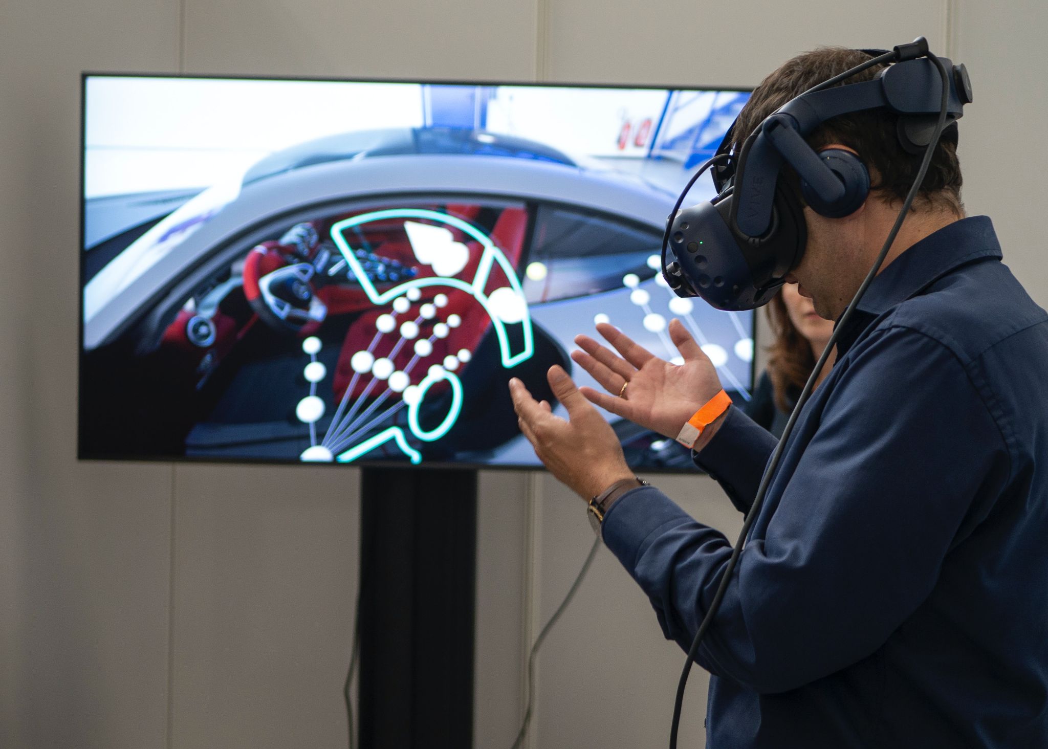 A man wearing VR goggles in front of a TV screen featuring a car