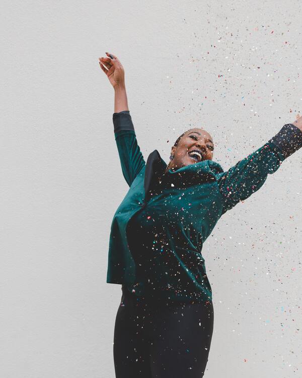 foto de uma mulher negra alegre e comemorando com papéis coloridos caindo em cima dela 