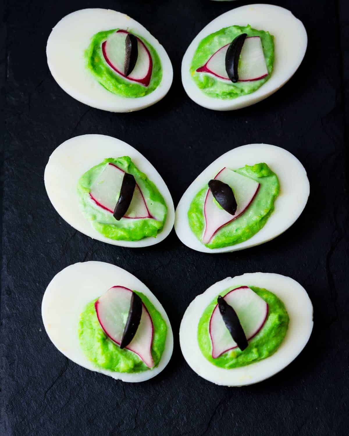 Healthy Halloween treats - deviled eggs designed to look like spooky eyeballs on a black background.