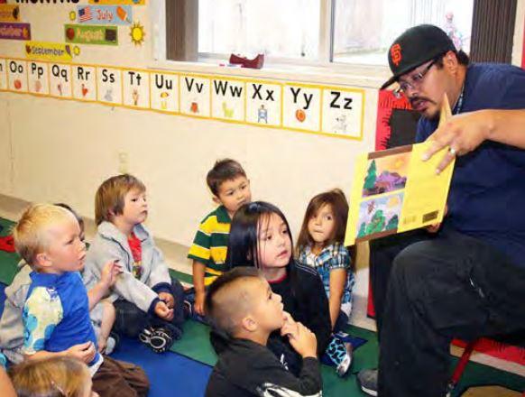 Teacher reading from a picture book to a group of children sitting on the floor around him