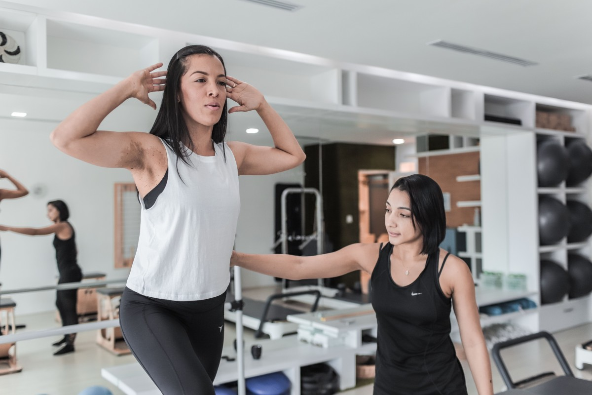 Two women in a gym, one teaching the other how to exercise