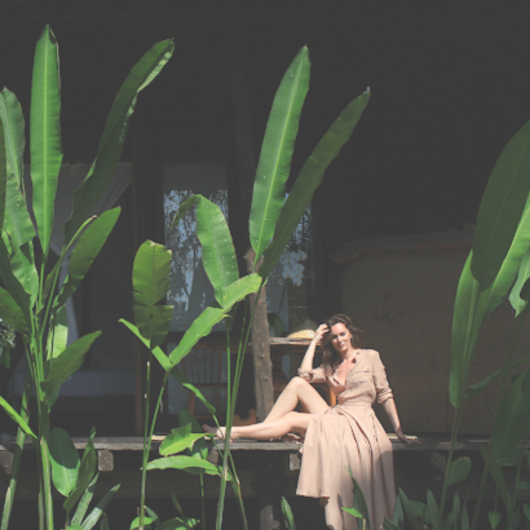 Woman in a nude dress posing amidst huge green plants
