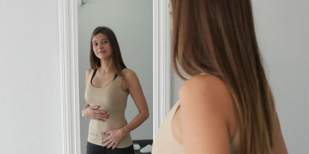 Une femme heureuse regardant ses seins nouvellement opérés dans le miroir après une chirurgie mammaire en Tunisie.
